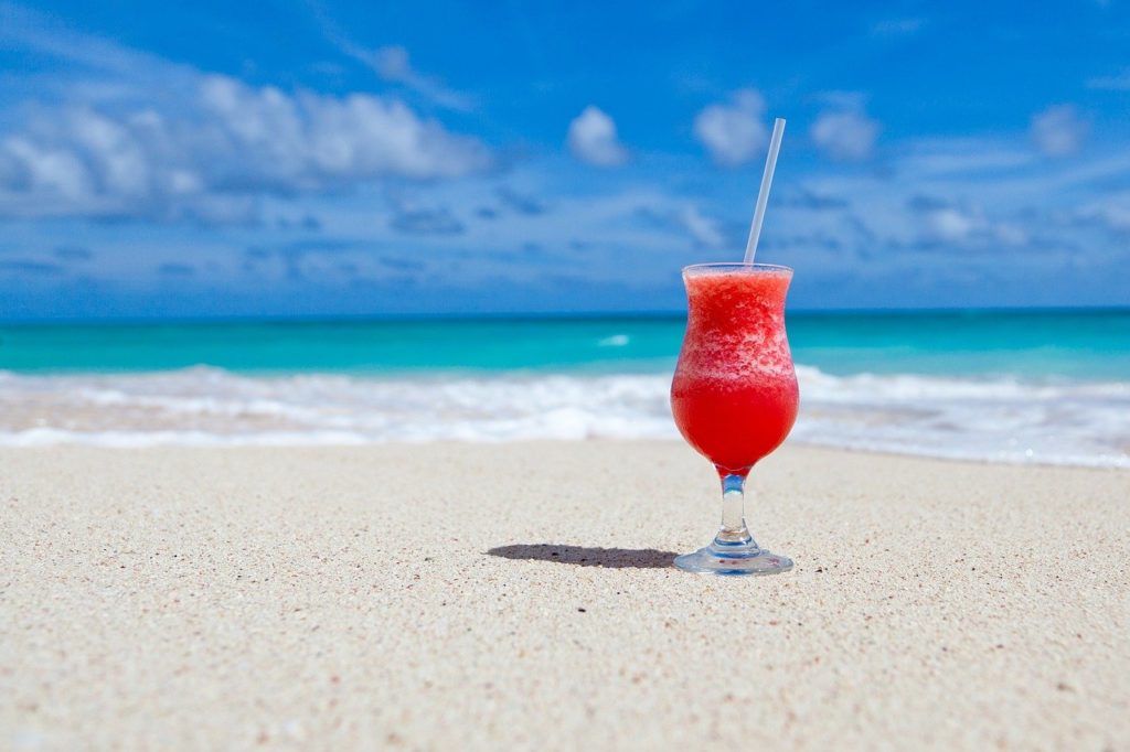 Vaso de Cocktail sobre la arena de una playa con el mar de fondo