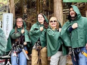 Una familia de cuatro personas, vestidas con capas verdes y posando con el puño sobre el corazón al estilo de los eldianos