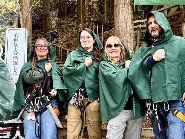 Una familia de cuatro personas, vestidas con capas verdes y posando con el puño sobre el corazón al estilo de los eldianos
